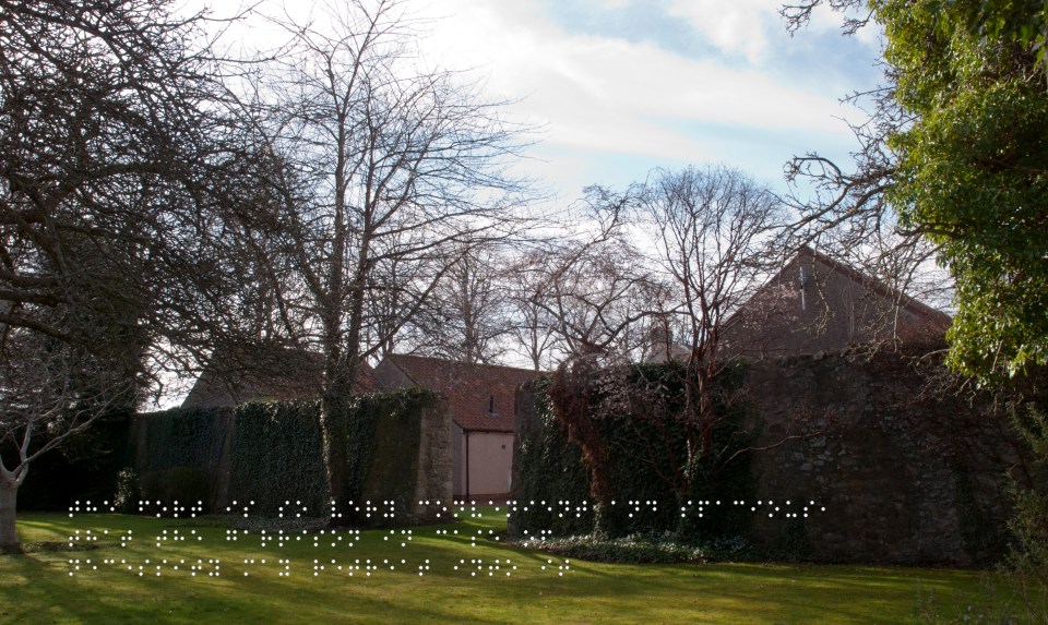 Bailey wall, now separating houses from a green space. Quote taken from historical figure shown in Braille